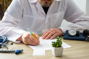 Doctor in white coat at workplace in hospital office seeing patients and fills medical documentations history of disease with focus on hand of physician. Scene with daily work of doctors with patients