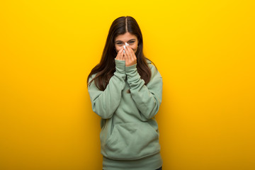 Teenager girl with green sweatshirt on yellow background smiling a lot while covering mouth