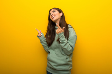 Teenager girl with green sweatshirt on yellow background pointing with the index finger and looking up