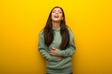 Obraz na płótnie Canvas Teenager girl with green sweatshirt on yellow background smiling a lot while putting hands on chest