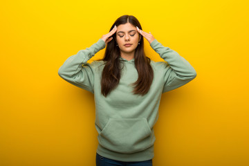 Teenager girl with green sweatshirt on yellow background unhappy and frustrated with something