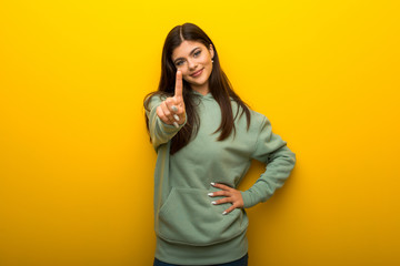 Teenager girl with green sweatshirt on yellow background showing and lifting a finger