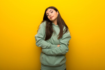 Teenager girl with green sweatshirt on yellow background making doubts gesture while lifting the shoulders