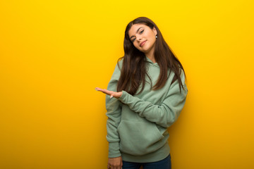 Teenager girl with green sweatshirt on yellow background presenting an idea while looking smiling towards