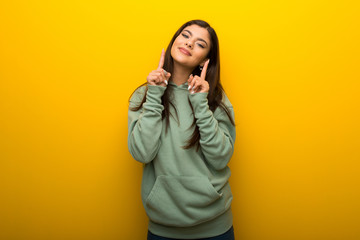 Teenager girl with green sweatshirt on yellow background smiling with a happy and pleasant expression