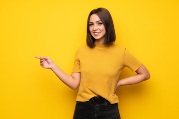 Young woman over yellow wall pointing finger to the side