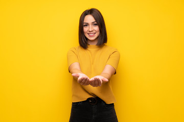 Young woman over yellow wall holding copyspace imaginary on the palm to insert an ad
