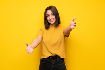 Young woman over yellow wall presenting and inviting to come with hand