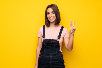 Young woman over yellow wall smiling and showing victory sign