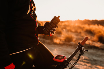 unrecognizable Cyclist holding water canteen on the bike on a Down Rocky Hill at Sunset. Extreme...