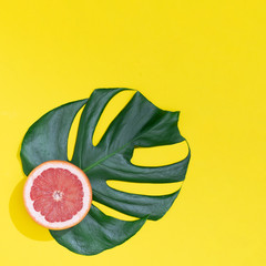Fototapeta na wymiar Monstera leaf with Red grapefruit on bright yellow background. Minimal summer concept.
