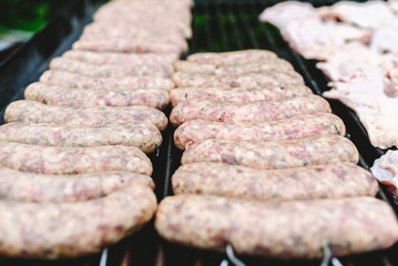 Many white sausages in a row to roast on a barbecue with charcoal.