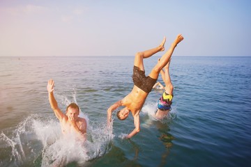 Young people jumping inside ocean in summer excursion day. Happy crazy friends diving from sailing...