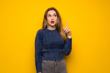 Teenager girl over yellow wall thinking an idea pointing the finger up