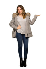 A full-length shot of a Teenager girl with coat holding copyspace imaginary on the palm to insert an ad on isolated white background