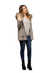 A full-length shot of a Teenager girl with coat saluting with hand with happy expression on isolated white background