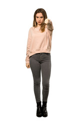 A full-length shot of a Teenager girl with pink sweater showing thumb dowg with negative expression over isolated white background