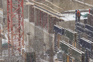 Building under construction in a snowfall close-up. Worker stands on the edge of a concrete structure