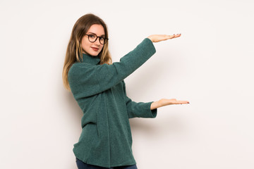 Teenager girl over white wall holding copyspace to insert an ad