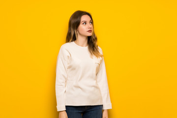 Teenager girl over yellow wall looking up with serious face