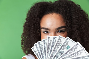 Pretty young african woman posing isolated over green wall background holding money.