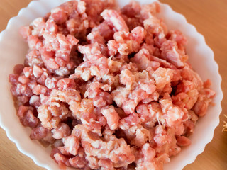 Minced pork in a white plate. Located on the kitchen table.