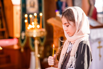 Little girl with a candle prays in church with eye closed