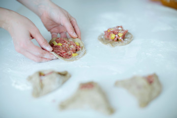 The girl carefully and gently sculpts meat pies. hands closeup on the table with flour
