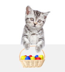 Fototapeta na wymiar Kitten with colorful Easter eggs in basket above white banner. Isolated on white background