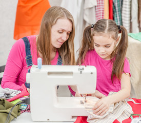 Woman teaches a little girl to sew on a sewing machine