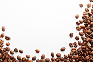 Roasted brown coffee beans scattered on white table with a lot copy space for text. Flat lay composition. Close up, top view, background.