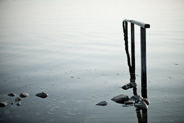 Relaxing background of a reflective surface with a Handrail disappear in the water and a view stones 
