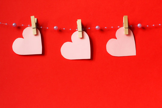 Three light pink hearts, hanging on the line, with wooden buckles, red background, free copy space, selective focus