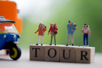 Miniature people : Traveler with backpack standing on wooden word TOUR with nature background