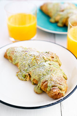 Pistachio croissants served on white and blue plates with orange juice. White wooden table, high resolution