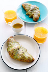 Pistachio croissants served on white and blue plates with orange juice. White wooden table, high resolution