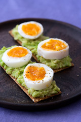 Rye sourdough crisp sandwiches with mashed avocado, boiled eggs. Served on a dark wooden plate, high resolution