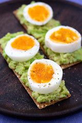 Rye sourdough crisp sandwiches with mashed avocado, boiled eggs. Served on a dark wooden plate, high resolution