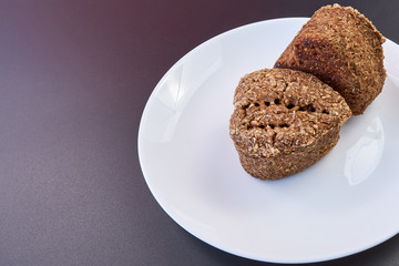 high quality dietary homemade bread two rolls on a white plate and a dark background. healthy food on the table. fresh bread. copy space