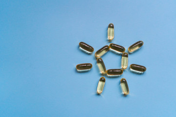 Close up capsules of fish fat oil in the sun shape, omega 3, vitamin e on the blue background....