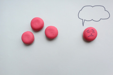 Three pink macaroons and sad face with copy space thoughts on a light background.