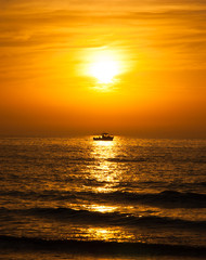 Naklejka na ściany i meble Silhouette of the fisherman or leisure boat sailing toward golden sunset with saturated sky and clouds. Beautiful seascape in the evening. Harmony with nature idea. Tranquility and freedom background.