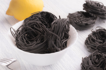 Black pasta in a white plate on a white table background.