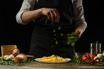 The chef sprinkles spicy herbs, parsley, french fries ready, on the background with vegetables. Cooking tasty but harmful food. Background for design and menu, home-made recipe, cookbook. Fast food