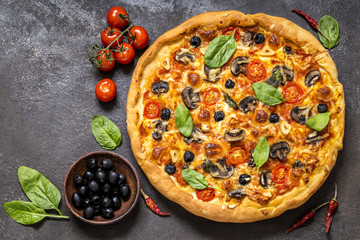 pizza with tomatoes, cheese, mushrooms, olives and spinach on a dark background