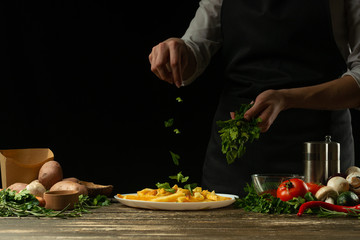 The chef sprinkles spicy herbs, parsley, french fries ready, on the background with vegetables. Cooking tasty but harmful food. Background for design and menu, home-made recipe, cookbook. Fast food