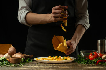 The chef pours into the envelope the french fries ready, freeze, on the background with vegetables. Cooking tasty but harmful food. Background for design and menu, home-made recipe. Fast food