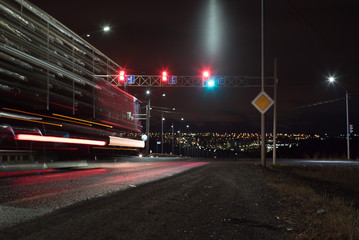 Time exposure photo with a street at night and automobile headlights and traffic light.