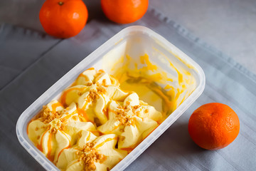 Orange ice cream with almond crumb and orange sauce in a plastic box.