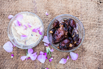 Close up shot of popular Indian & Asian winter dessert in a transparent glass bowl i.e. Khajor ka halwa or dates confection with raw dates and some rose petals on brown colored surface.